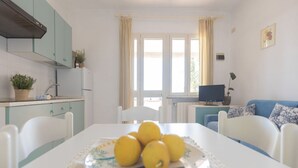 Un coin repas avec une table dressée pour quatre personnes, une cuisine en arrière-plan et une fenêtre avec des rideaux.