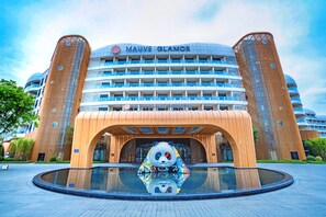 Un hotel con una llamativa escultura de panda en primer plano, un amplio frente de vidrio y un diseño arquitectónico moderno.