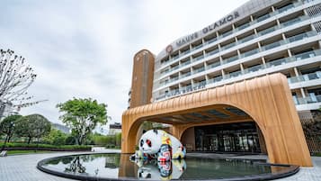 Um edifício moderno com uma grande estátua de panda na entrada, um lago refletor e um céu claro.