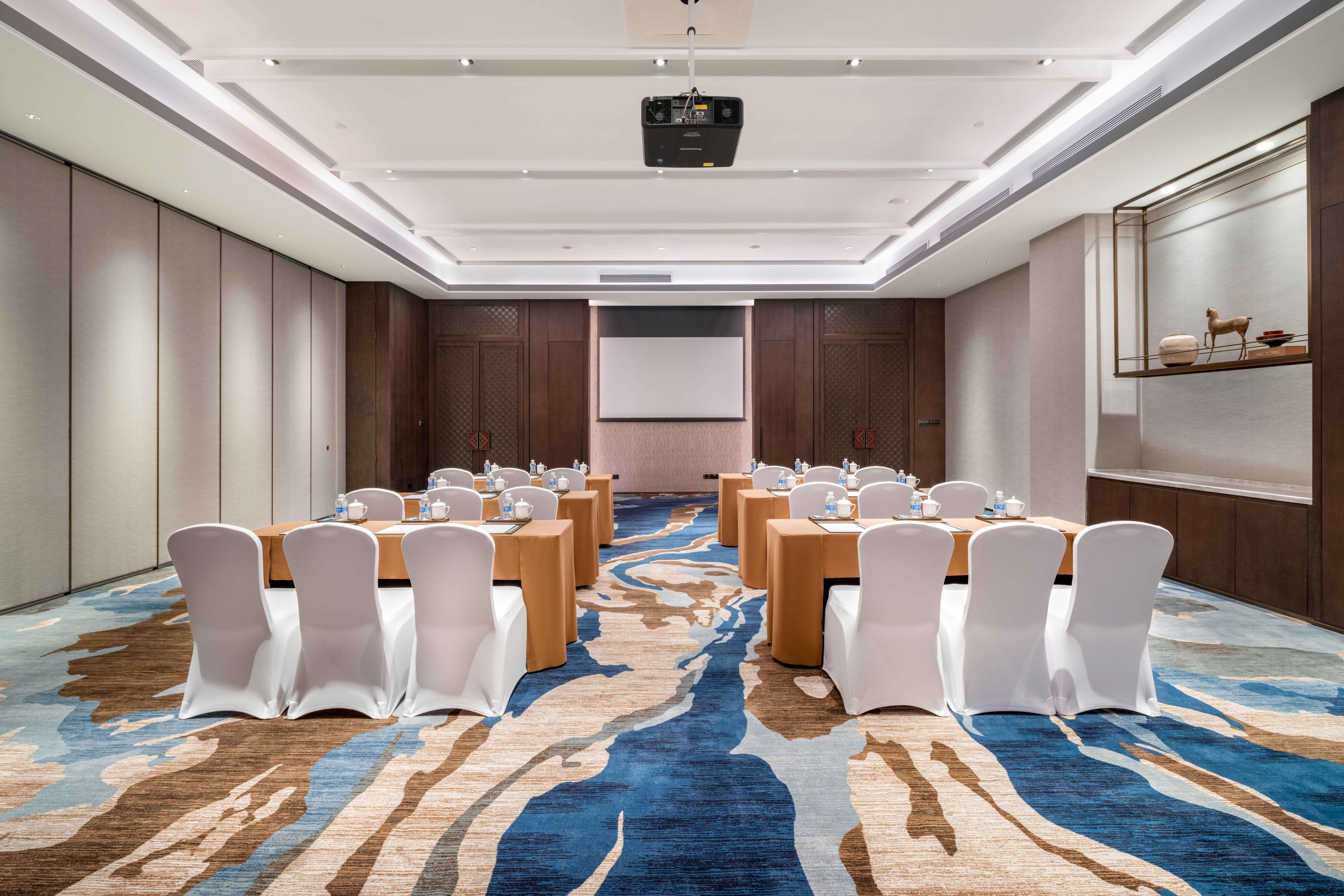 A conference room with a large screen, white chairs, and a patterned carpet.