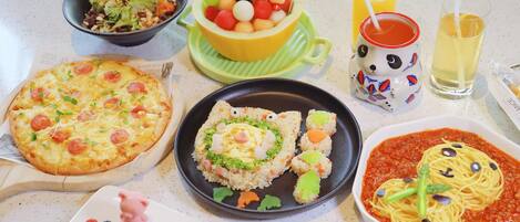 A variety of food items on a table, including pizza, sushi, pasta, and a bowl of fruit.