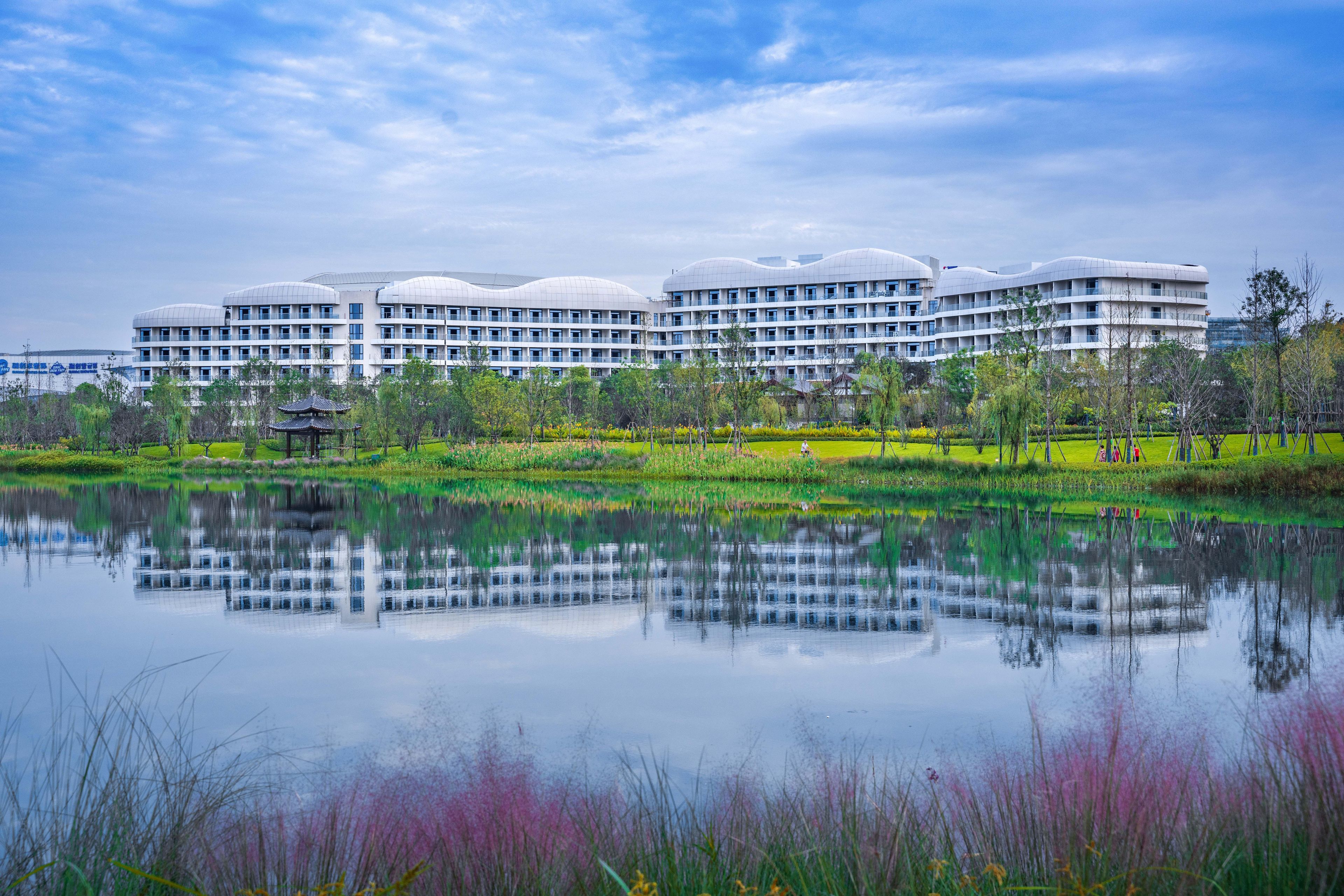 A modern hotel with multiple floors and a reflection in a calm lake.