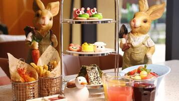 A table with a tiered dessert stand, a duck figurine, and various food items.