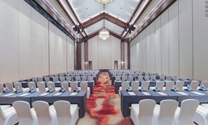 A conference room with rows of tables and chairs, a patterned carpet, and a high ceiling with a chandelier. - Mauve Glamor Chengdu (Chengdu)