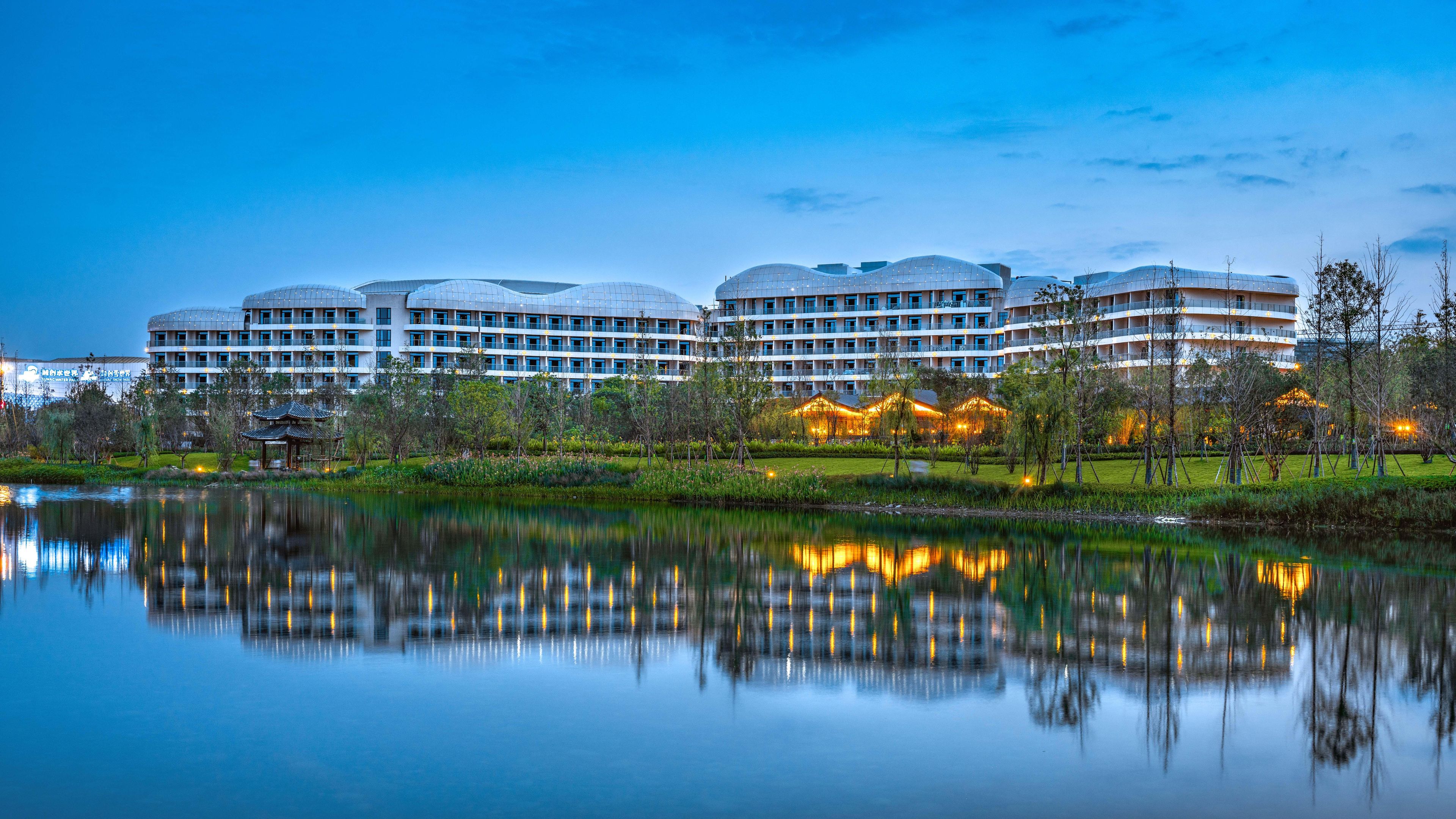Un hotel moderno con varias construcciones en forma de cúpula, un lago que se refleja y un jardín bien cuidado.