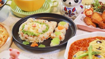 A table with various dishes, including a bear-shaped dessert, a plate of rice with vegetables, and a bowl of soup.