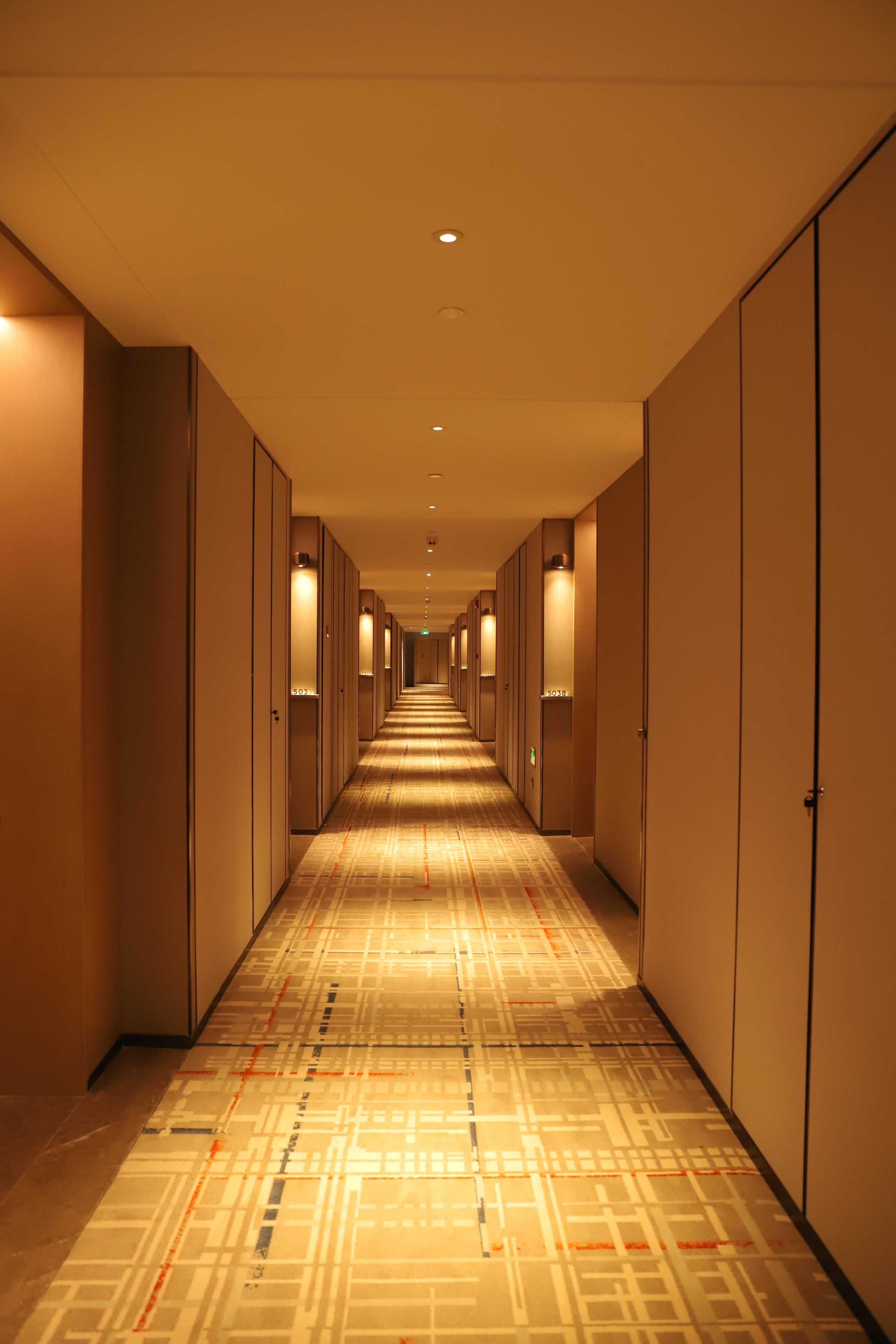 A hotel corridor with a patterned floor, doors on both sides, and overhead lighting.