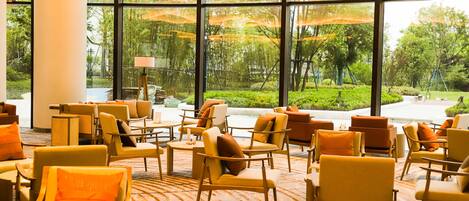 Un hall de hotel con amplios ventanales, varias zonas de estar y vistas a un jardín.