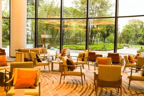 A hotel lobby with large windows, multiple seating areas, and a view of a garden. - Mauve Glamor Chengdu (Chengdu)