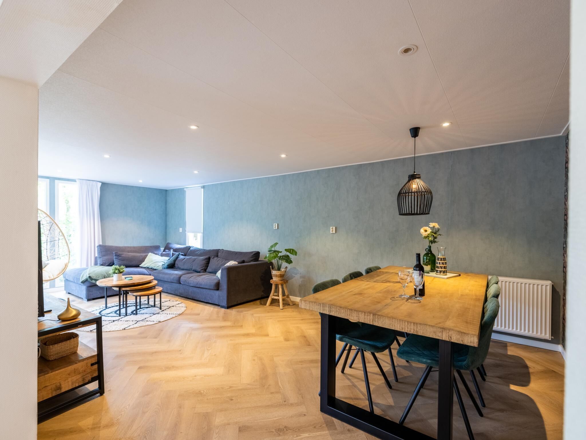 Een moderne woonkamer met een bank, salontafel, eettafel en een hanglamp.