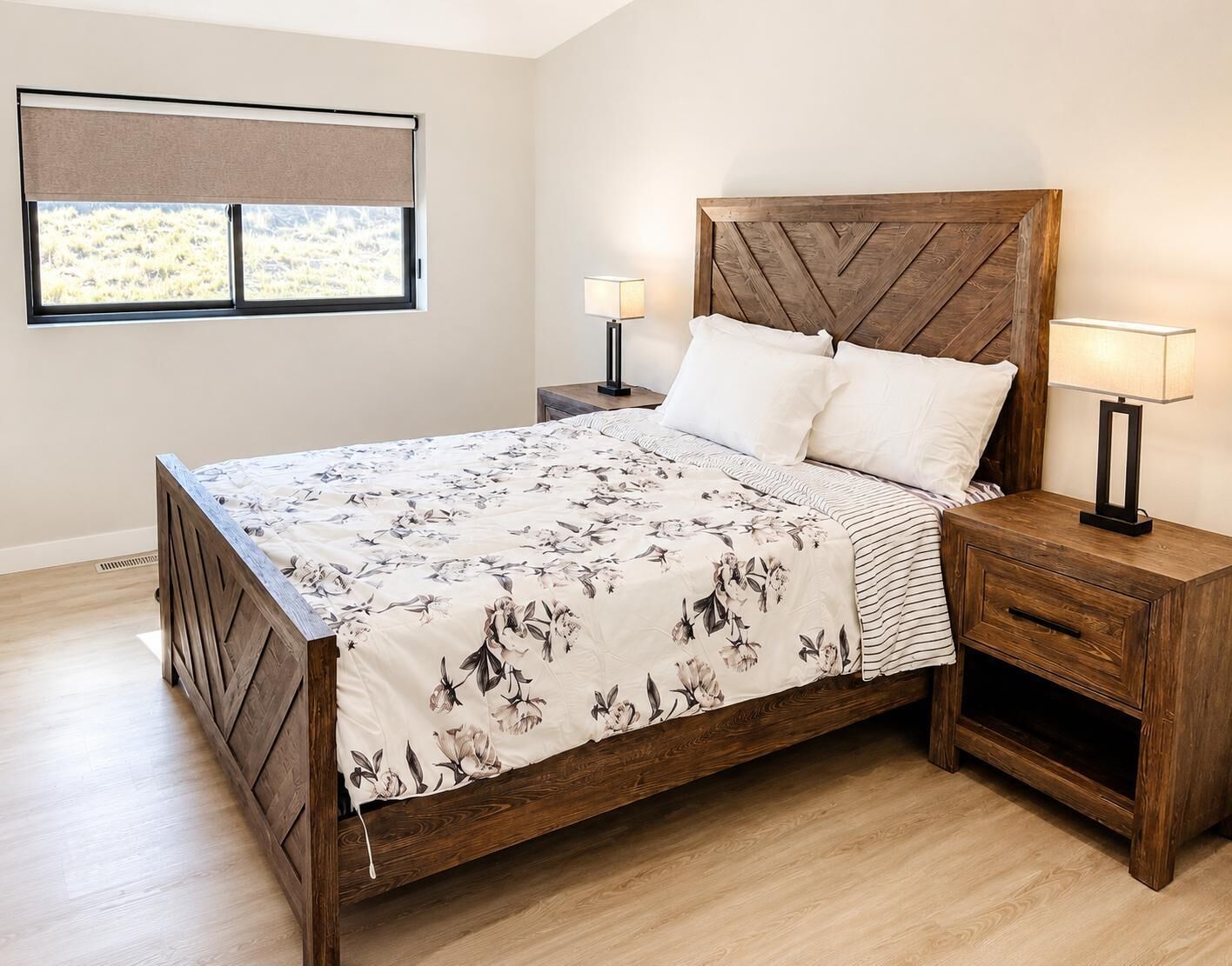 A bedroom with a wooden bed, two bedside tables with lamps, a window with a view, and a wooden floor.