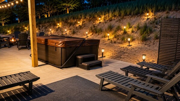 Un bain à remous avec une terrasse en bois, des chaises longues et des guirlandes lumineuses, le tout aménagé dans un espace extérieur paysager.