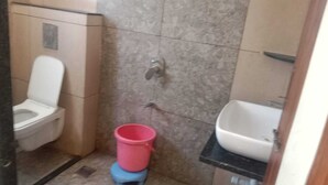 Un bagno piccolo con il water, un lavandino e un secchio rosa su uno sgabello.