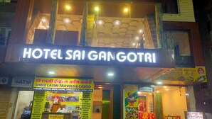 Un hotel chiamato 'Hotel Sai Gangotri', con una insegna e una pubblicità di agenzia di viaggi.