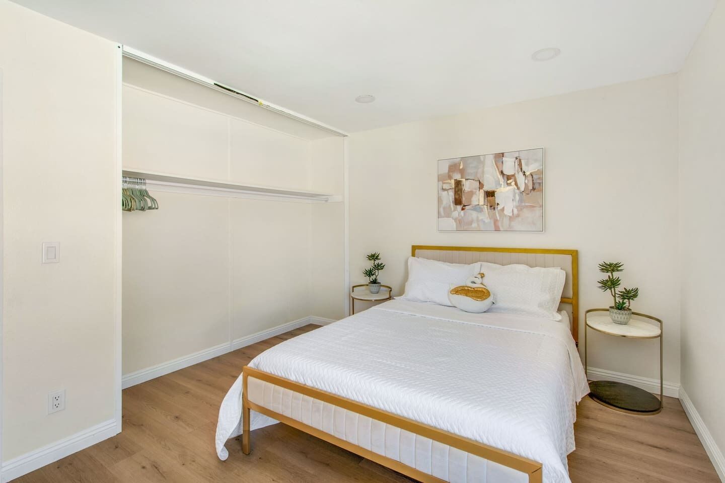 Un dormitorio con una cama de madera, ropa de cama blanca, un estante montado en la pared y dos mesitas de noche con plantas.