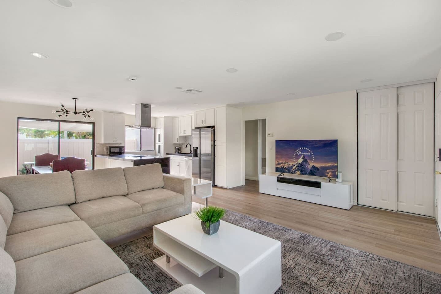 A modern living room with a sofa, a coffee table with a plant, a flat-screen TV, and a kitchen in the background.