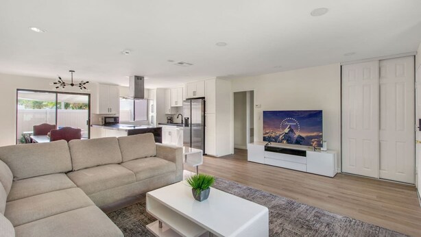 Ein modernes Wohnzimmer mit einer Couch, einem Couchtisch mit Pflanze, einem Flachbildfernseher und einer Küche im Hintergrund.