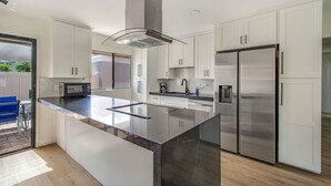 Eine moderne Küche mit weißen Schränken, einem Edelstahlkühlschrank und einer großen Kochinsel mit Glasplatte.