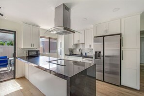 A modern kitchen with white cabinets, a stainless steel refrigerator, and a large island with a glass top.