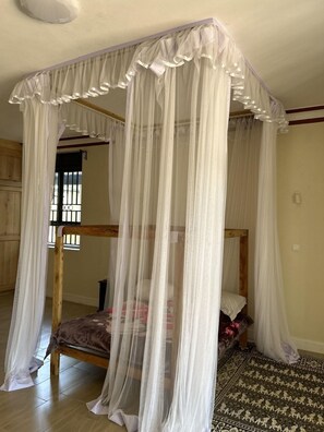 A room with a four-poster canopy bed, wooden flooring, and a patterned rug. - Ridgeway Victoria (Entebbe)