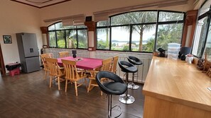 A dining area with a wooden table and chairs, a bar counter with stools, and large windows offering a view of palm trees and a distant landscape. - Ridgeway Victoria (Entebbe)