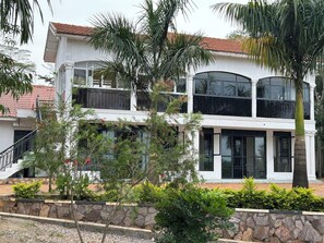 A two-story building with a white facade, large windows, and a stone retaining wall. - Ridgeway Victoria (Entebbe)
