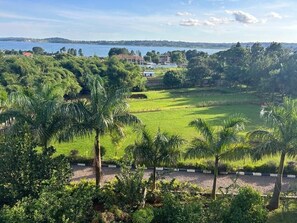 A lush green landscape with palm trees, a clear sky, and a body of water in the distance. - Ridgeway Victoria (Entebbe)