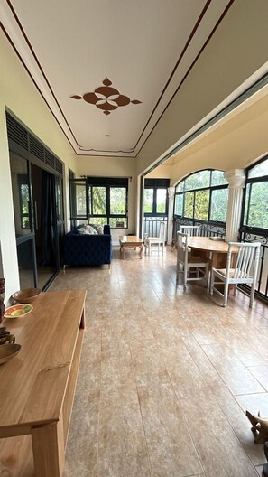 Een ruime kamer met een grote eettafel, een bank en uitzicht door grote ramen.
