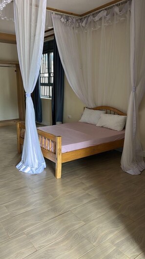 A single bed with a wooden frame and a pink mattress, surrounded by white curtains. - Ridgeway Victoria (Entebbe)