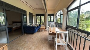 Een balkon met een eettafel en stoelen, een bank en een bed in de aangrenzende kamer.