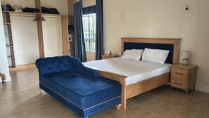 A bedroom with a bed, a blue sofa, a wooden wardrobe, and a window with curtains. - Ridgeway Victoria (Entebbe)