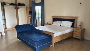 A bedroom with a bed, a blue sofa, a wooden wardrobe, and a window with curtains. - Ridgeway Victoria (Entebbe)