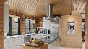 A modern kitchen with wooden walls, a stainless steel refrigerator, and a wooden table with fruit. - Forest retreat with sauna & nearby beach (Højby)