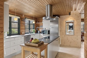 A modern kitchen with wooden walls, a stainless steel refrigerator, and a wooden table with fruit. - Forest retreat with sauna & nearby beach (Højby)