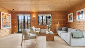 A log cabin interior with a sofa, armchair, and a table with a vase. - Forest retreat with sauna & nearby beach (Højby)