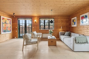 A log cabin interior with a sofa, armchair, and a table with a vase. - Forest retreat with sauna & nearby beach (Højby)