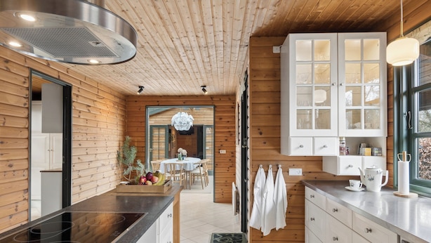 A modern kitchen with wooden walls, a black countertop, and a dining area with a chandelier. - Forest retreat with sauna & nearby beach (Højby)
