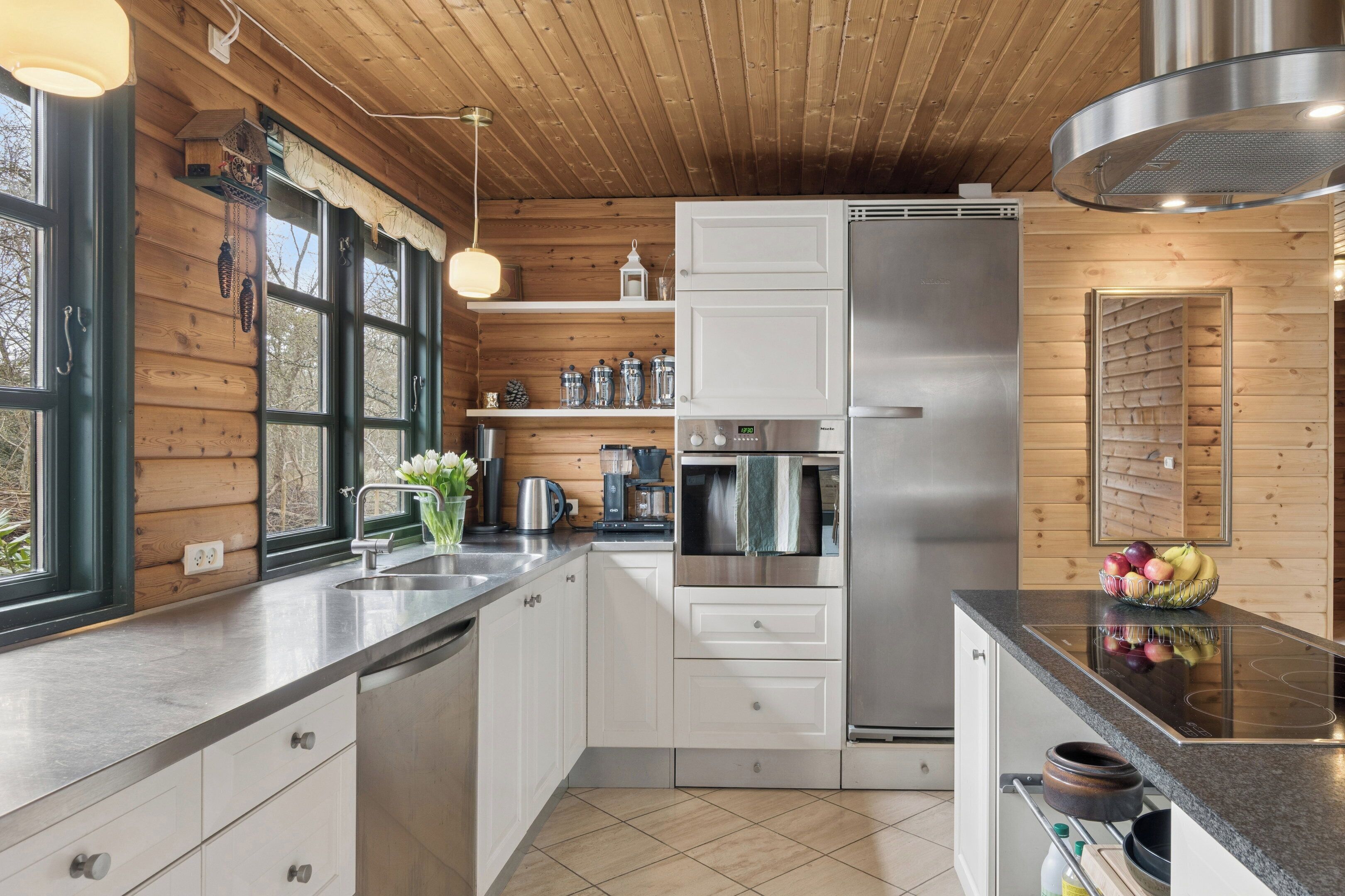 A modern kitchen with wooden walls, stainless steel appliances, and a large window.
