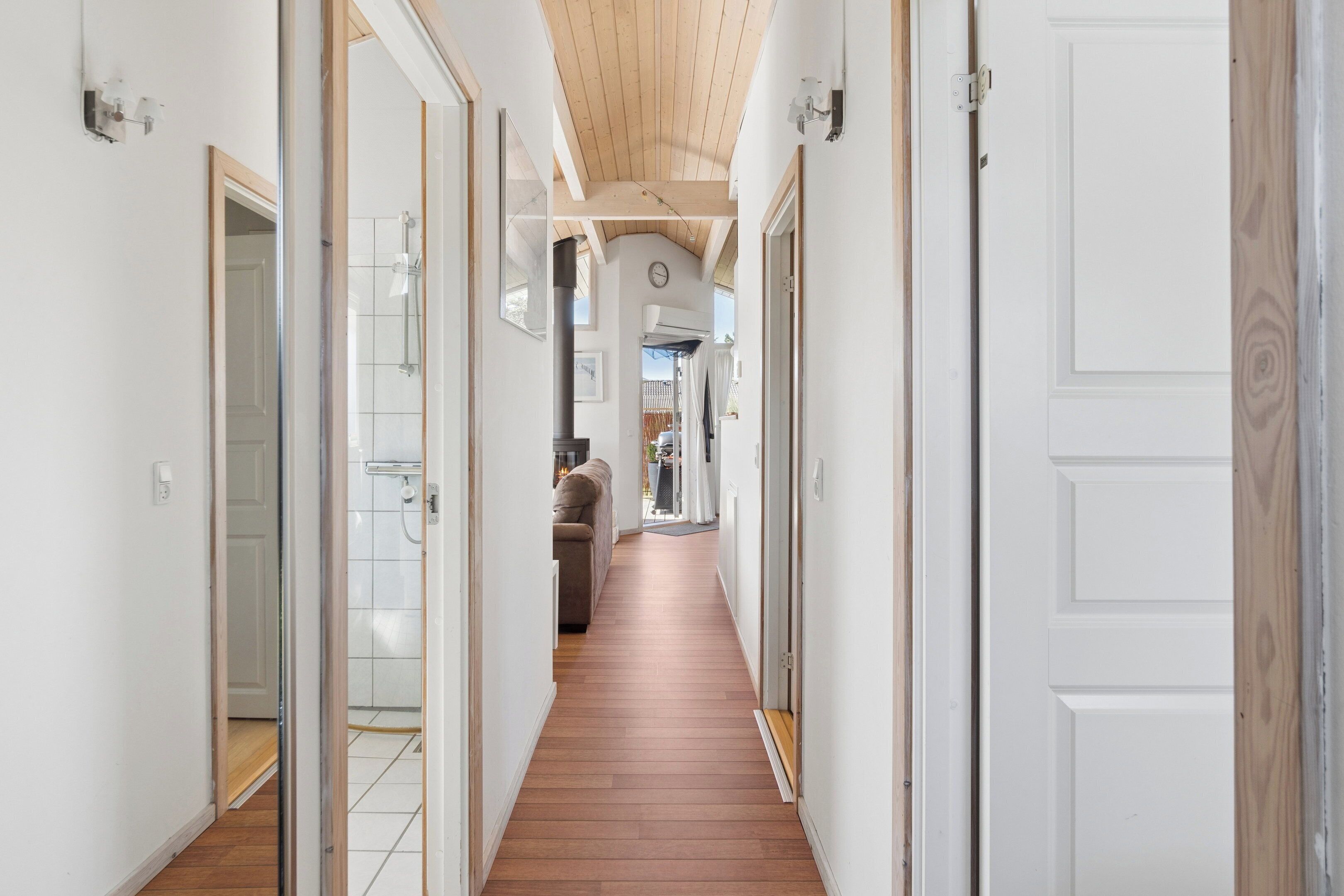 Un couloir doté d’un plancher en bois, de murs blancs et de portes donnant accès à différentes pièces.