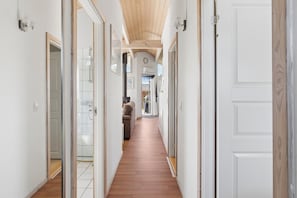 Un pasillo con piso de madera, paredes blancas y puertas que dan a diferentes habitaciones.