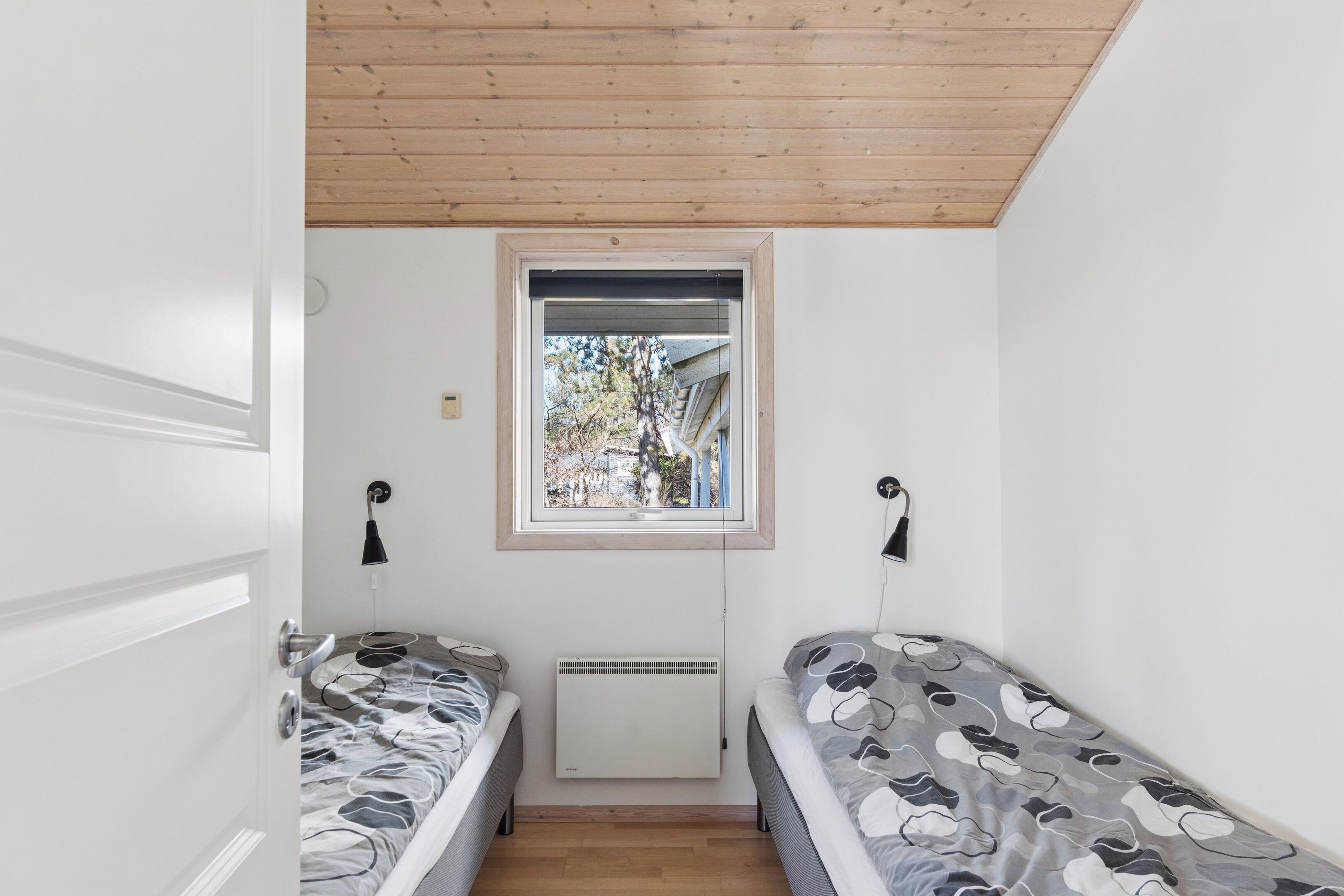Une petite pièce avec deux lits, une fenêtre, un radiateur et une porte.