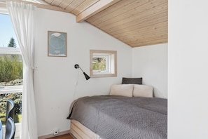 A bedroom with a bed, a window, a wall-mounted lamp, and a framed picture.
