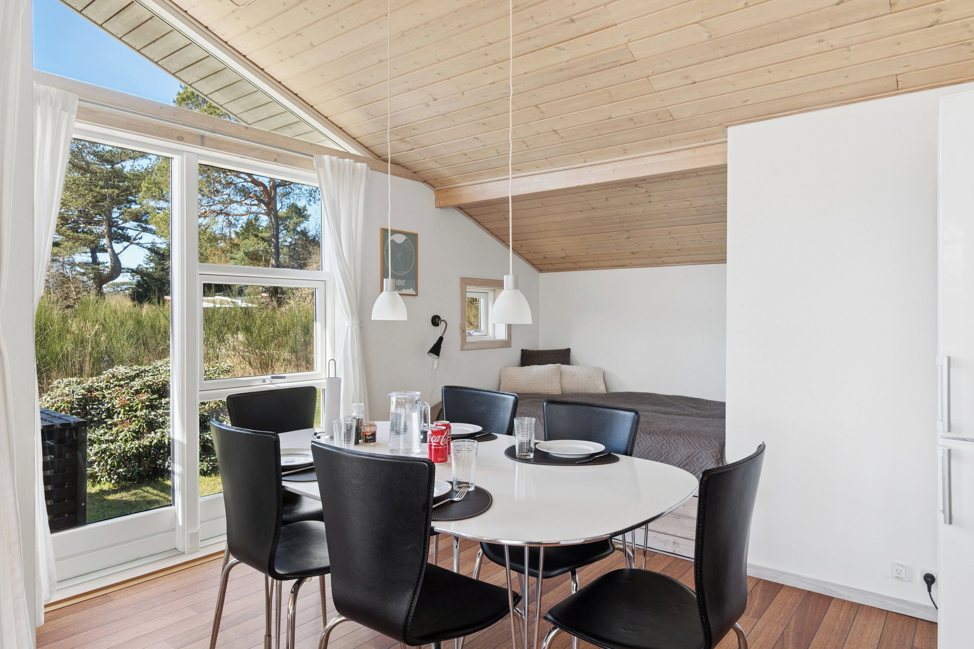Un espace repas avec une table ronde, des chaises noires et une vue sur l’extérieur.