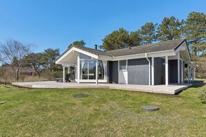 A modern house with a covered patio, large windows, and a grassy yard.