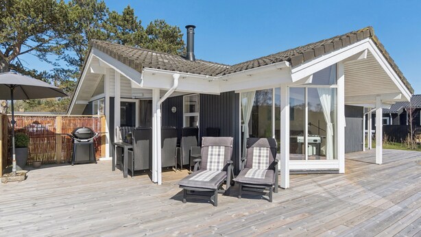 A covered outdoor area with two lounge chairs, a barbecue grill, and a pergola structure.