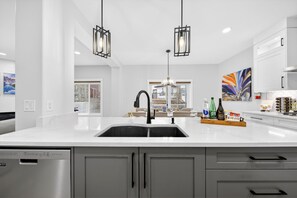 Een moderne keuken met een wit aanrecht, een RVS vaatwasser, grijze kastjes en hanglampen.