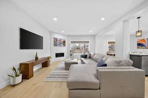 Een moderne woonkamer met een grote flatscreentelevisie, een bank, een houten bankje en een potplant.