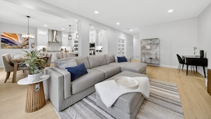 A modern living room with a sectional sofa, a dining area, and a kitchen in the background. - Modern Luxury 6BR Home •Sleeps12•12 mins Airport (Calgary)