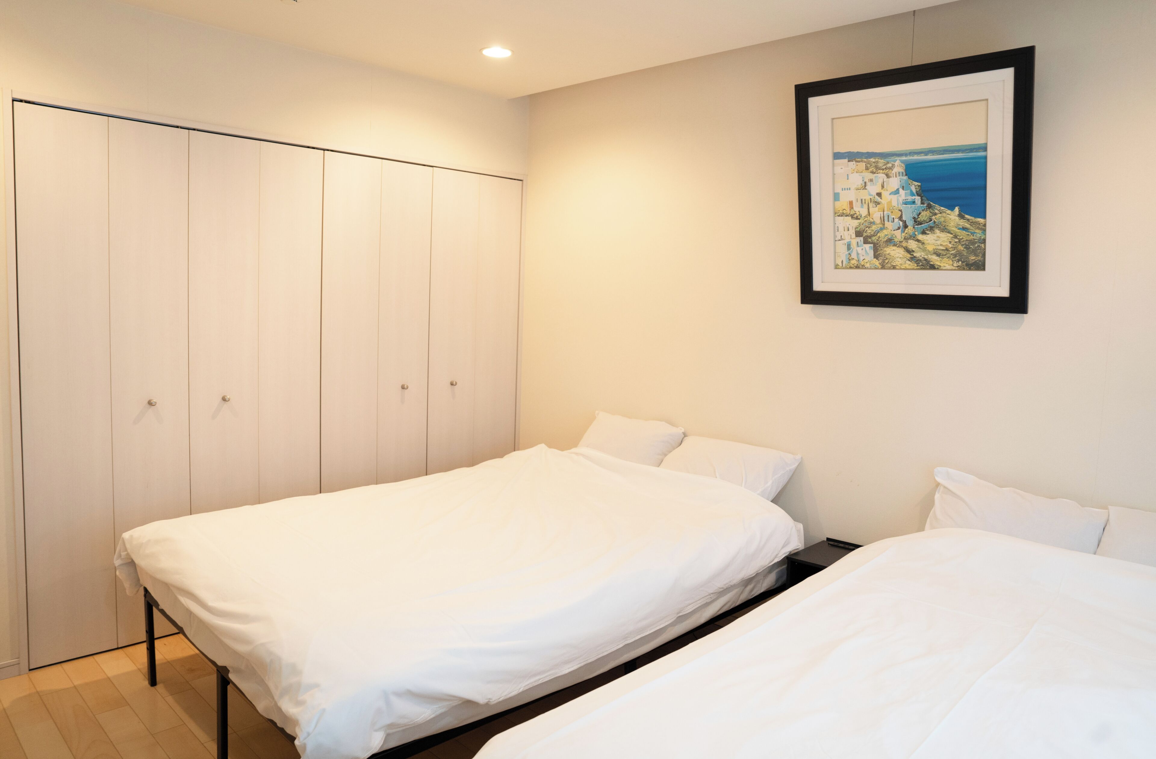 Une chambre avec deux lits, une armoire et un tableau encadré au mur.