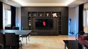 Ein modernes Wohnzimmer mit Flachbildfernseher, dunklen Holzböden, einem Esstisch mit Stühlen und einem Ledersofa.